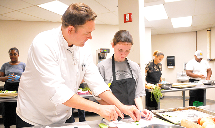 Chef Robert Gerstenecker assists a student in the Academy for Learning and Social Growth with knife skills in the KSU Center Culinary kitchen