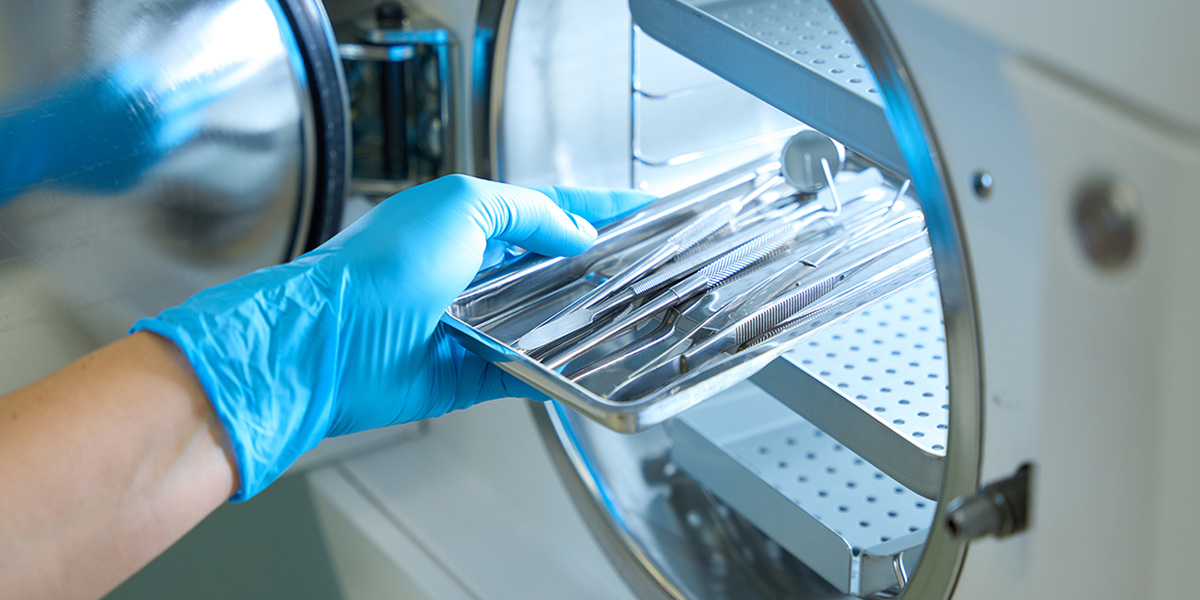 Sterile processing technician placing a sterilized instrument tray into an autoclave